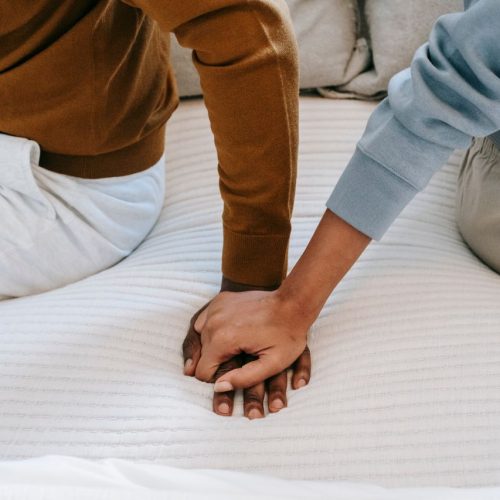 Crop faceless African American couple sitting on bed back to back and holding hands